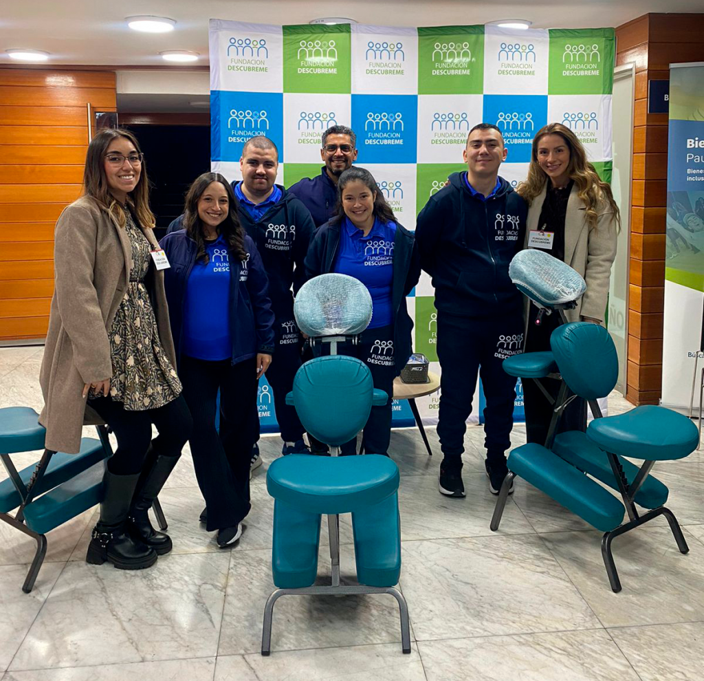 Siete integrantes del equipo de Bienestar Inclusivo posan junto a sillas de masoterapia durante el encuentro empresarial organizado por CAMACOES.