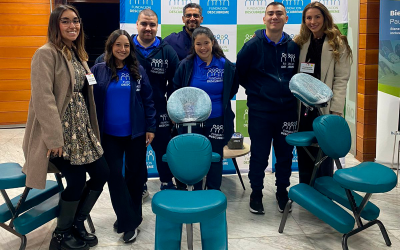 Siete integrantes del equipo de Bienestar Inclusivo posan junto a sillas de masoterapia durante el encuentro empresarial organizado por CAMACOES.